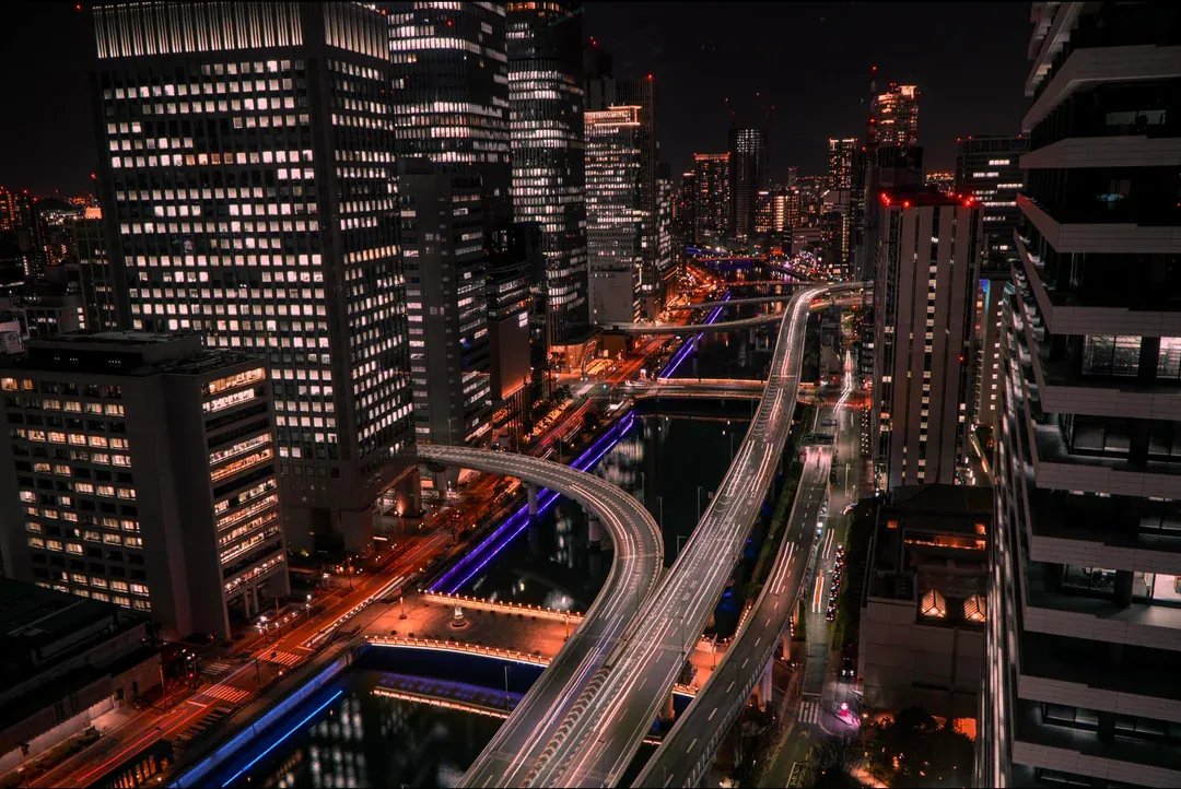 Long-exposure light trails tracing elevated expressways curving between illuminated glass towers.