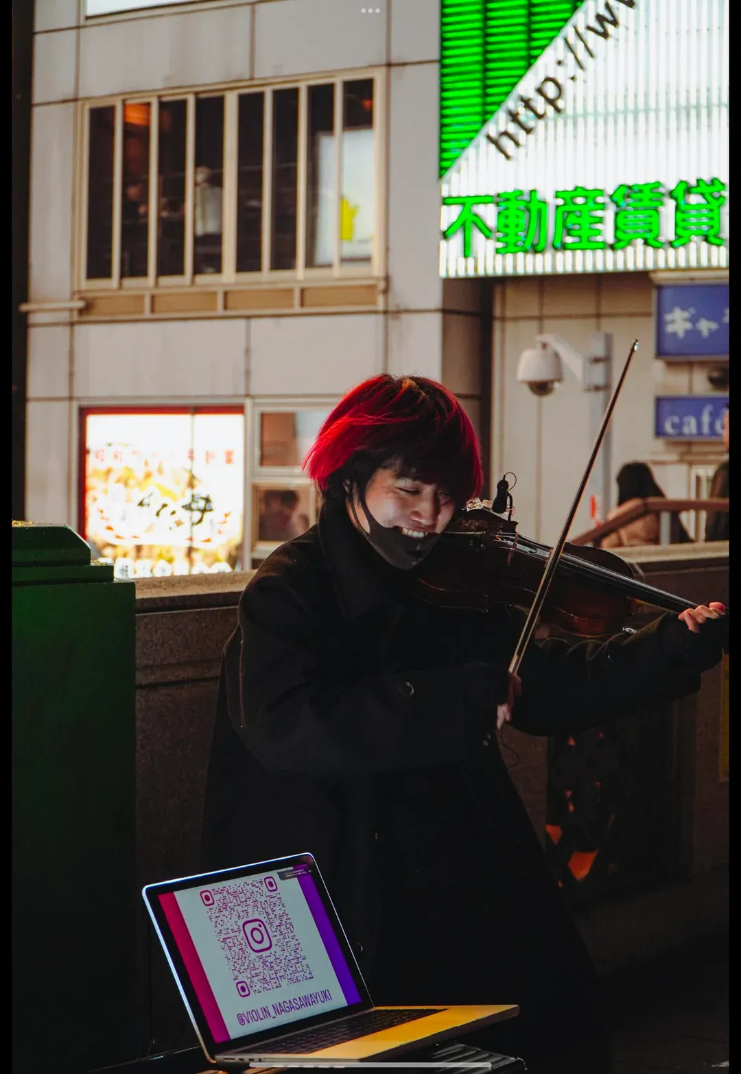A street musician on electric violin against the glow of late-night signboards.